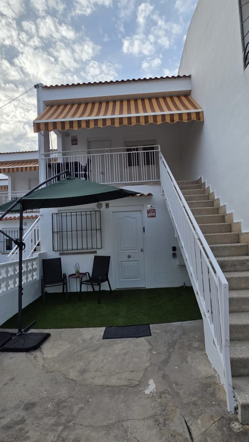 Bungalow blanco con toldo a rayas, patio privado con césped artificial y barandillas metálicas en Benicàssim, España