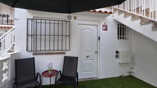 Terraza privada de la casita Monica Socarici en Benicàssim con asientos, césped verde, puerta blanca y ventana con rejas negras