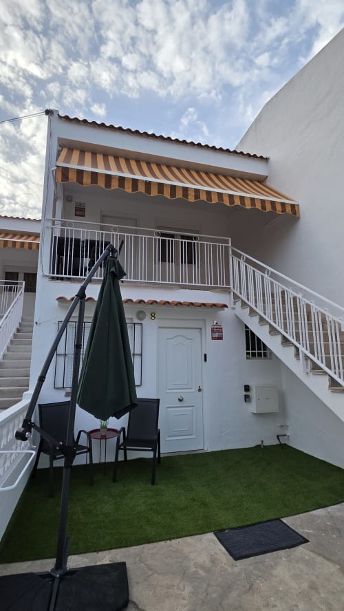 Bungalow blanco con toldo amarillo, terraza privada con sombrilla negra y sillas en Benicàssim, España
