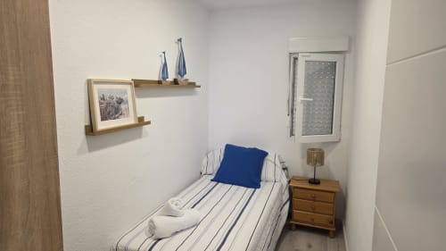 Acogedora habitación en bungalow frente al mar de Oropesa con ropa de cama a rayas, almohada azul, mesita de noche de madera y decoración náutica