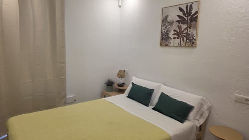 Dormitorio moderno y luminoso en casita de Benicàssim con ropa de cama amarilla, almohadas blancas, cojines verde oscuro y lámpara de mesita