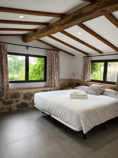 Rustic bedroom at El Escondite De Pedro Malillo with exposed wooden beams, white ceiling, stone walls, and views of Candeleda