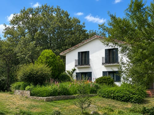 White rural cottage with dark shutters surrounded by lush gardens and trees in Candeleda, Spain