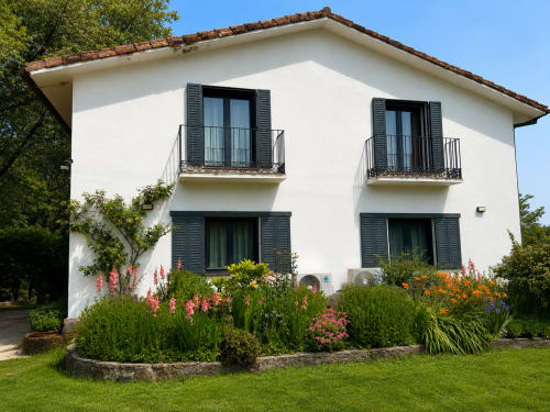 White two-story villa with dark shutters, terracotta roof, and colorful garden in Candeleda, Spain