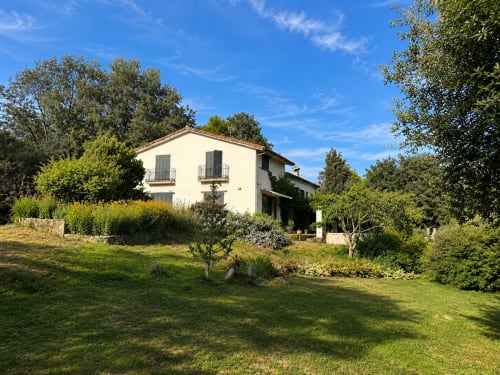 Rustic white villa with green shutters surrounded by lush gardens and trees in Candeleda, Spain