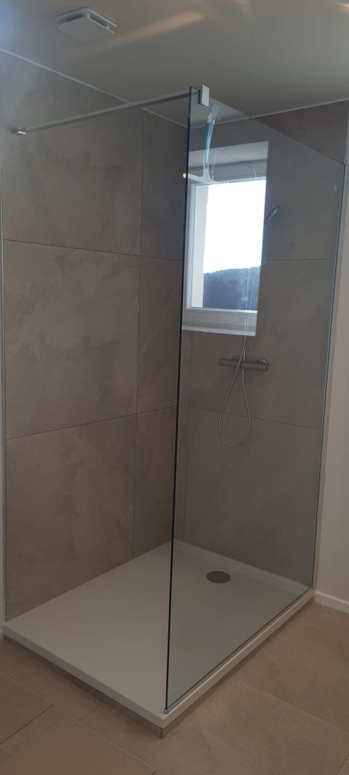 Douche moderne en verre avec murs en carrelage marron et pluie de tête dans la salle de bain de l'appartement Les Gîtes d'Avalon
