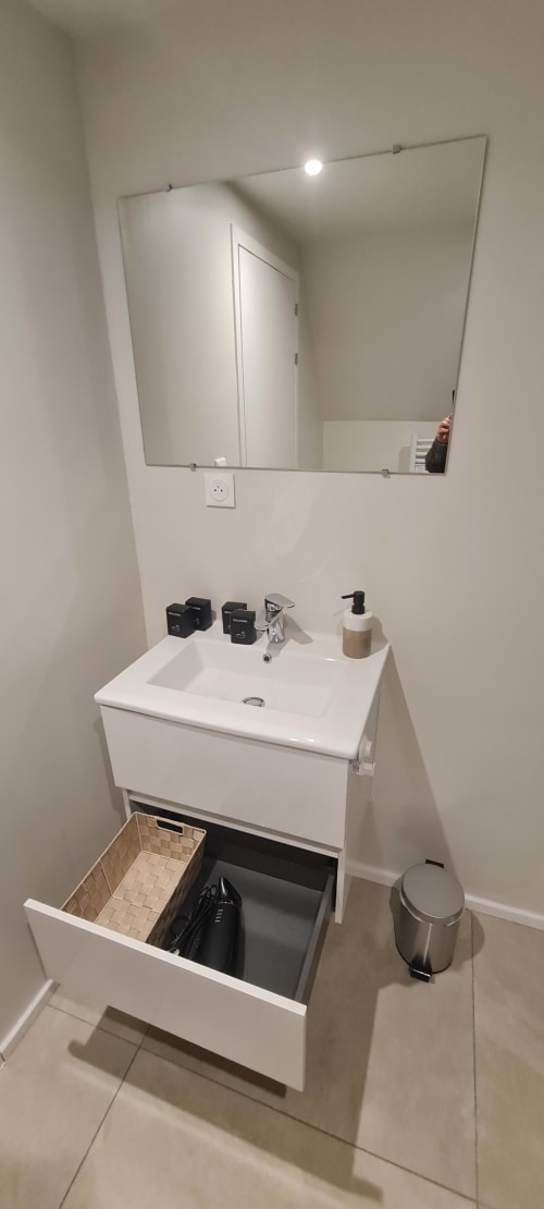 Salle de bain moderne aux Gîtes d'Avalon avec lavabo blanc, miroir et rangements à Thannenkirch