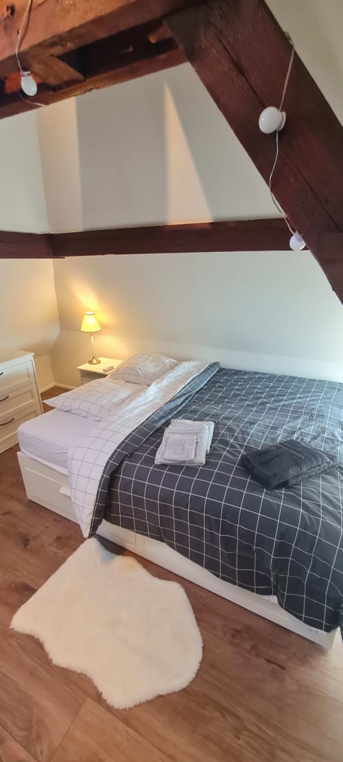 Chambre sous les combles cosy aux Gîtes d'Avalon avec lit queen-size, poutres en bois, lampe de chevet et vue sur les montagnes à Thannenkirch