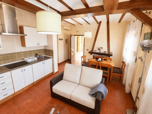 Amplia sala de estar de la villa en Finca El Arroyo con sofá crema, vigas de madera, cocina abierta, mesa de comedor y terracota