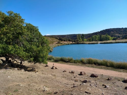 Vista panorámica del lago en Finca El Arroyo, Alcaraz, con árboles verdes, colinas, agua turquesa y playa de arena