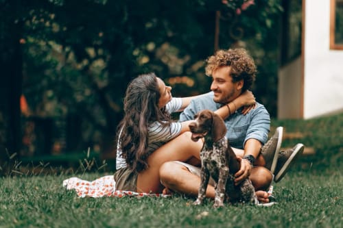 Pareja relajándose en el jardín del hotel Holibai en Baiona, España, con perro y fachada cubierta de hiedra de fondo