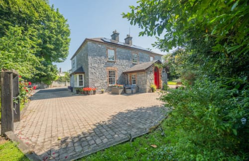 Stone villa at Knockaderry House in Ennis with red door, patio, lush gardens, and countryside views