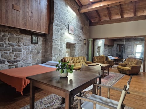 Salón rústico de piedra con sillones dorados y vigas de madera en el hotel rural Aldea Pazos De Arenteiro