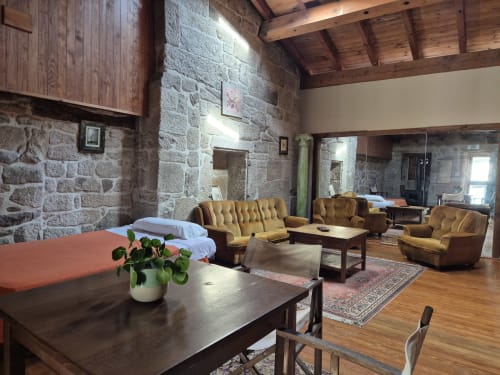 Amplio salón de piedra con sillones mostaza, vigas de madera y chimenea en Aldea Rural Pazos De Arenteiro