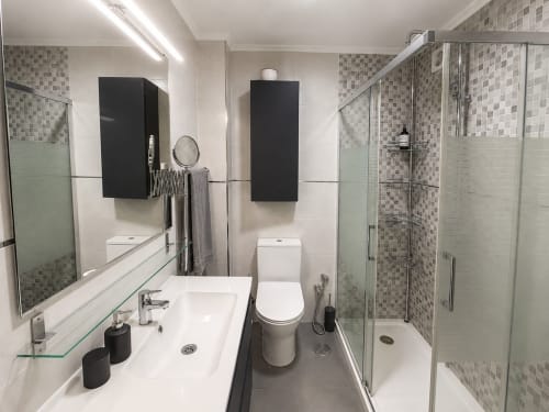 Baño moderno del hotel Holibai en Baiona con doble lavamanos, ducha con mampara de cristal y acentos de azulejos a cuadros