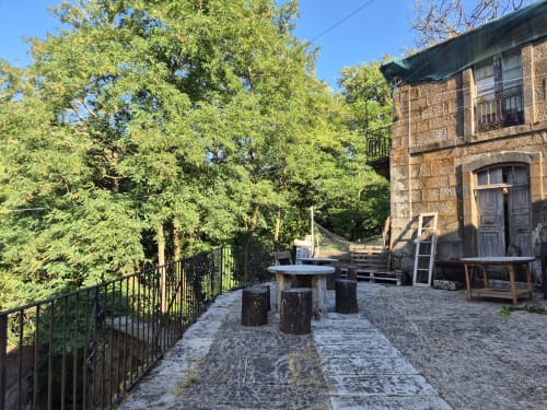 Patio rústico de Aldea Rural Pazos De Arenteiro con asientos de piedra, árboles frondosos y edificio tradicional de ladrillo en España
