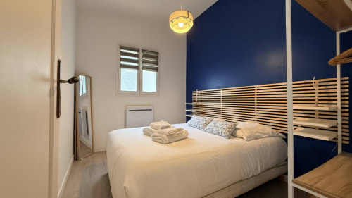Chambre moderne au Clos Bussy avec lit queen-size, mur d'accent bleu marine, lattes bois et luminaires contemporains.