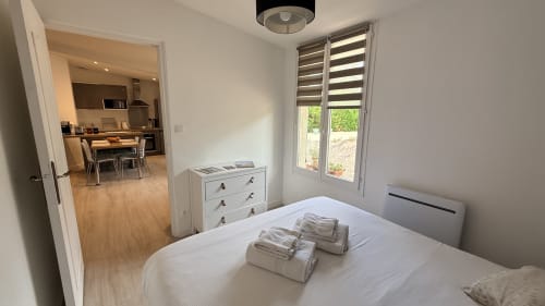 Chambre lumineuse du gîte Le Clos Bussy avec lit blanc, commode, fenêtres vue jardin et cuisine ouverte