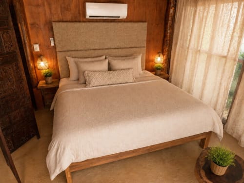 Cozy bedroom in Isla Mujeres cottage with beige bedding, wooden headboard, nightstands with lamps, AC unit, and garden view