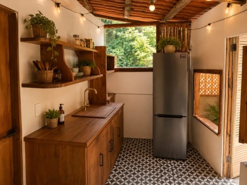 Modern tiny house kitchen in Isla Mujeres with wooden cabinets, stainless steel refrigerator, and garden view through windows