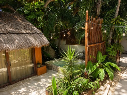 Tropical garden courtyard at Isla Mujeres cottage with thatched-roof bungalow, pool, lush plants, and wooden fence