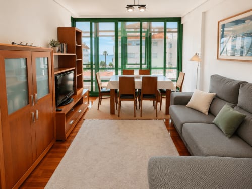 Moderno salón del hotel Holibai Baiona con sofá gris, muebles de madera y balcón con vistas al mar