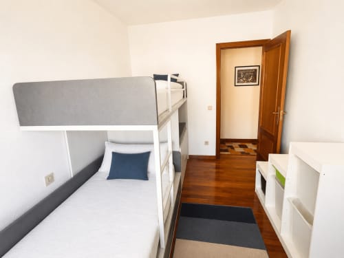 Habitación con camas litera en el hostel Holibai de Baiona: estructura blanca, piso de madera y entrada