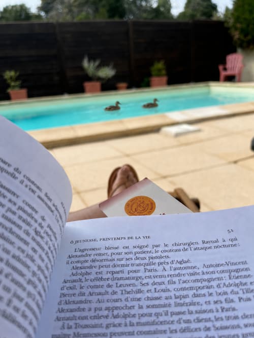 Hôte en lecture au bord de la piscine du gîte Le Clos Bussy à Bellerive-sur-Allier, canards nageant dans l'eau turquoise