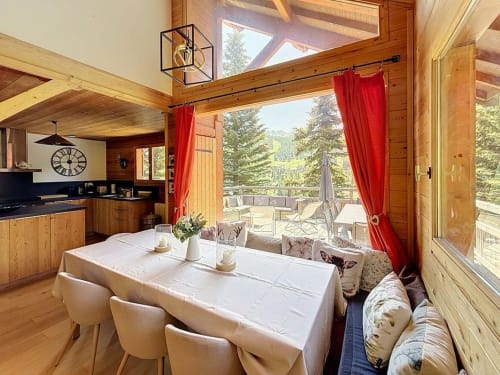 Spacieux séjour du chalet de Montgenèvre avec vue sur les montagnes, poutres en bois, rideaux rouges et accès à la cuisine moderne