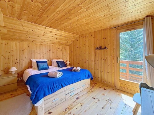 Chambre en bois du chalet de Montgenèvre avec literie bleue, murs en pin et balcon avec vue montagne