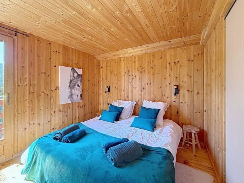 Chambre du chalet en bois aux Tanières avec literie turquoise, oreillers bleus et œuvres de loup à Montgenèvre