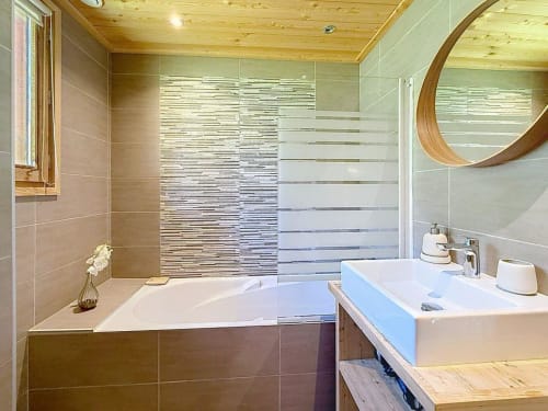 Salle de bain moderne du Chalet Eskimo aux Tanières de Montgenèvre avec baignoire, lavabo, plafond en bois et douche carrelée rayée