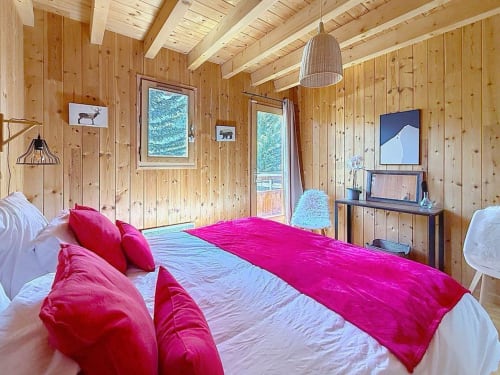 Chambre chaleureuse de chalet en bois avec literie rose, poutres apparentes et vue sur les montagnes aux Tanières de Montgenèvre