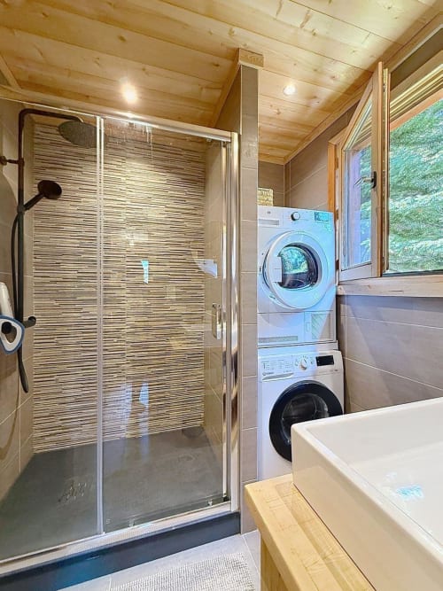 Salle de bain moderne dans chalet de Montgenèvre avec douche à l'italienne, lave-linge et sèche-linge superposés, baignoire balnéo et plafond en bois
