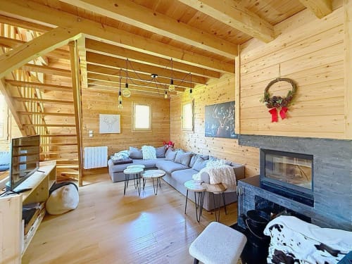 Salon chaleureux de chalet en bois avec foyer, canapé gris, suspensions et couronne festive à Montgenèvre