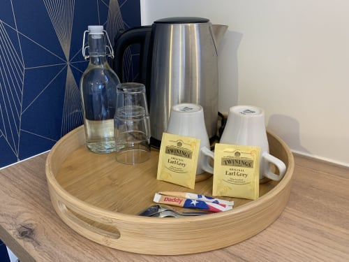 Plateau en bois avec thé Earl Grey Twinings, bouilloire électrique et carafe d'eau dans la chambre d'hôtes de La Maison Blanche Bouguenais