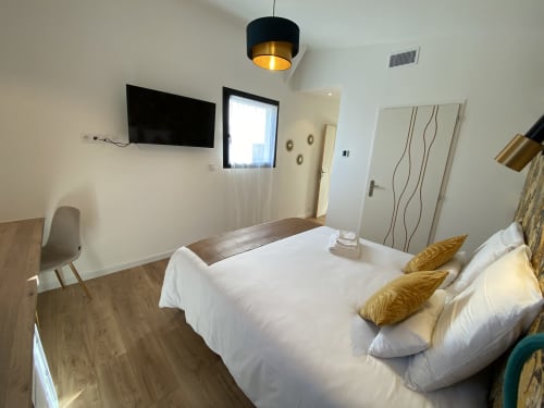 Chambre moderne de La Maison Blanche B&B à Bouguenais avec literie blanche, touches dorées et télévision écran plat