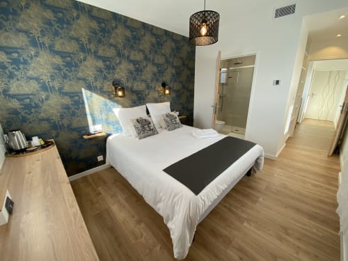 Chambre moderne à La Maison Blanche avec mur d'accent aux motifs bleus, lit blanc et salle de bains attenante à Bouguenais.