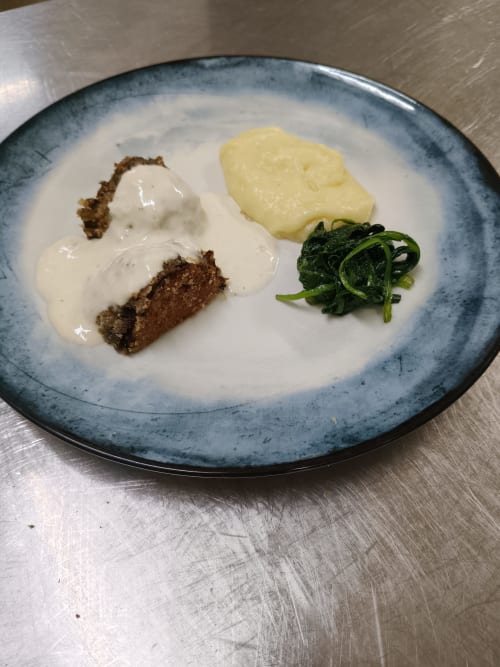 Elegant plated dish at Hotel Ristorante alle Querce in Castelbuono with meatloaf, creamy sauce, mashed potatoes, and spinach