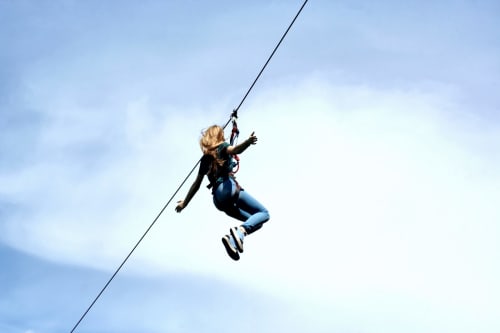 Person zip-lining against blue sky near Hotel Ristorante alle Querce in Castelbuono, Italy