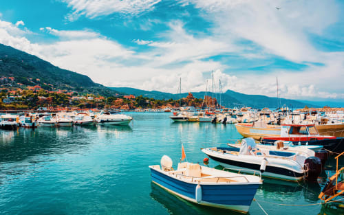Colorful fishing boats in turquoise Mediterranean harbor near Castelbuono, Italy with mountains and coastal town