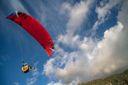 Paraglider soaring with red parachute over Castelbuono, Sicily mountains and blue sky