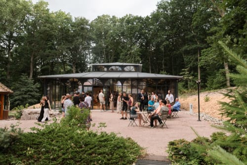 Modern glass pavilion at Les Jardins de Madeleine with guests mingling on terrace surrounded by forest, Bernardvillé