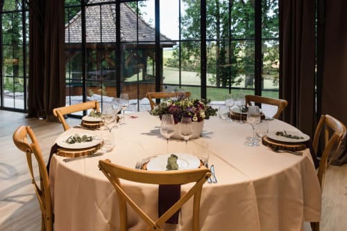 Elegant dining room at Les Jardins de Madeleine with round table, wooden chairs, and panoramic windows overlooking gardens in