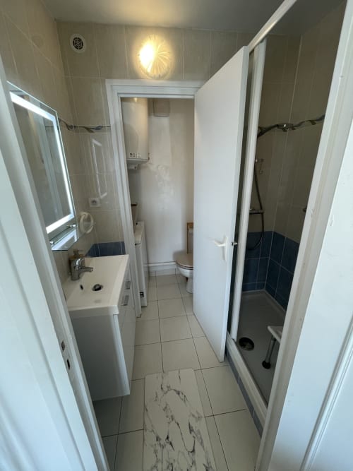 Couloir étroit de salle de bain au Studio L'île verte avec lavabo, toilettes et douche aux carrelages bleu foncé