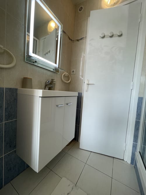 Salle de bain moderne avec vasque blanche, miroir rétroéclairé et murs carrelés au Studio L'île verte, Guimiliau