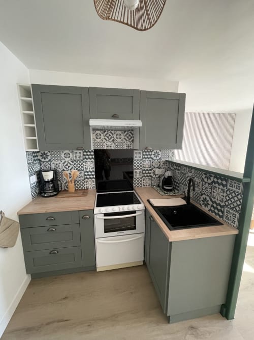 Cuisine moderne de l'atelier Parenthèse En Finistère avec façades vert sauge, carrelage à motifs, plan de travail bois et blanc