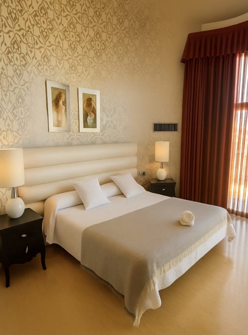 Elegante habitación en Hotel Villa de Cacabelos con ropa de cama crema, papel tapiz estampado, cortinas burdeos y comodidades modernas
