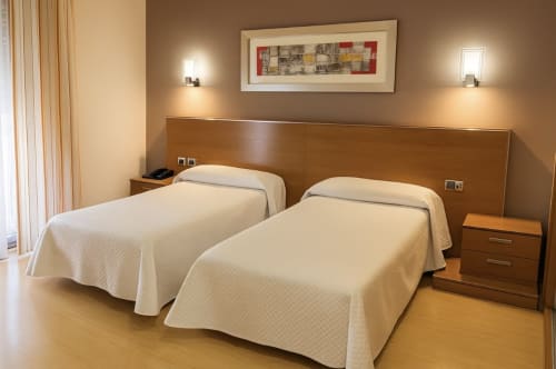 Habitación doble en Hotel Villa de Cacabelos con camas de madera, ropa de cama color crema e iluminación cálida en España