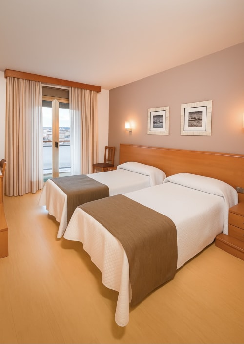 Habitación doble en Hotel Villa de Cacabelos con camas de madera, balcón con vistas a la ciudad y decoración cálida